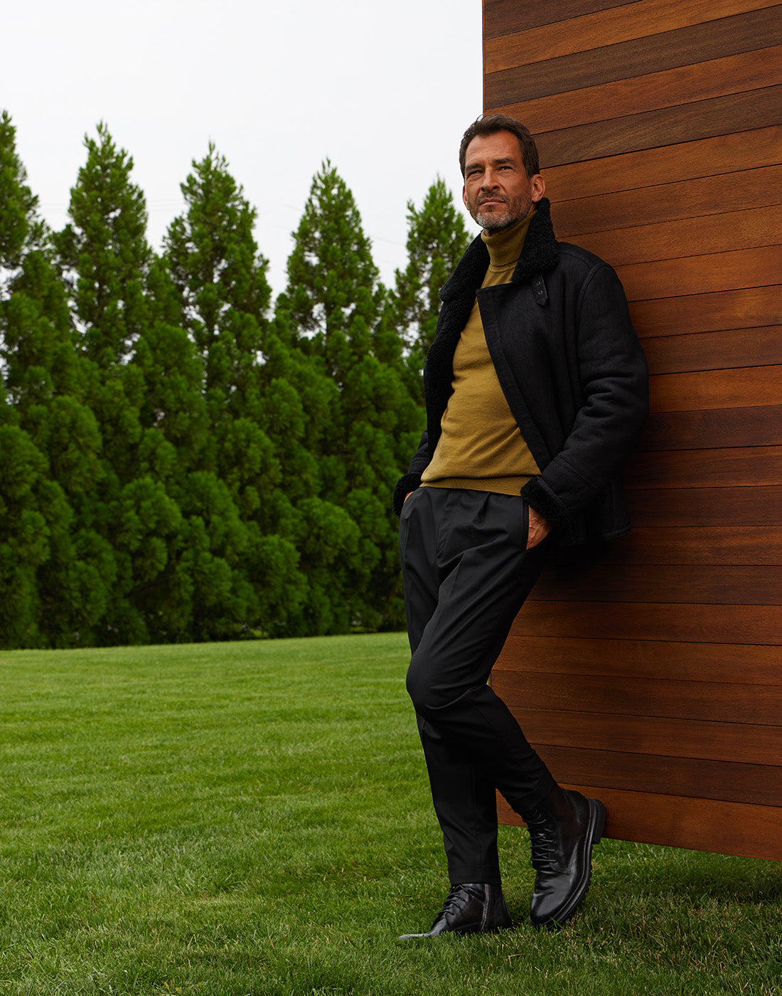 Man leaning against a wooden wall wearing the Edmundo boot in black